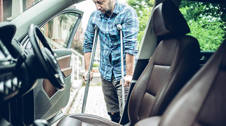 Man on crutches enters his car and is thankful he has Personal Injury Protection.